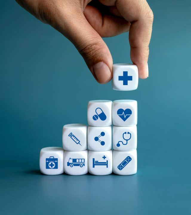 Healthcare medical, wellness plan and insurance concept. Health, care and medical element icon symbols on clean white blocks stacking as a graph arranged by doctor's hand on blue background.